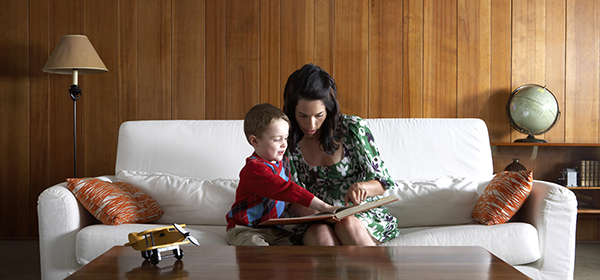 Mother and son (3-5) on couch, reading in living room