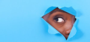 A view of a woman's eye looking through a hole in some colorful paper