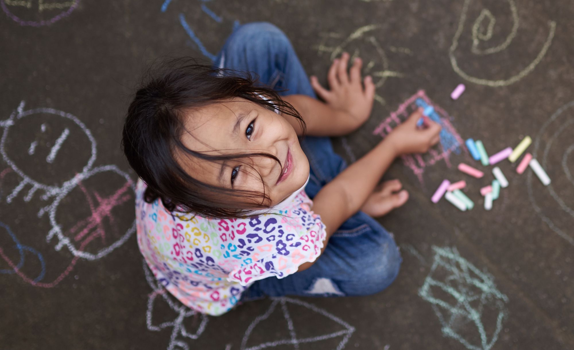 small girl with chalk on painted asphalt background above top view
