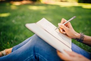Close up image of person writing in a notebook with grass in the background