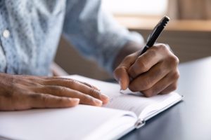 Man sits at a desk and writes in a journal 