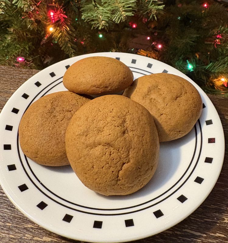 A color photograph of four golden brown ginger cookies sitting on a white plate