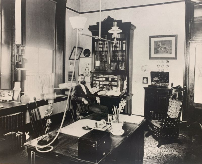 Black and white photo of Dr. CF Menninger seated at a secretarial desk in his offices at 727 S Kansas Ave