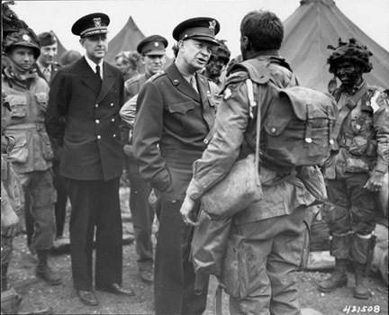 A black and white photo of General Dwight D. Eisenhower speaking with troops from the 101st Airborne before the D-Day invasion
