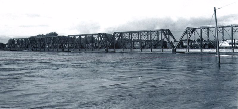 A black and white photograph showing the Santa Fe Railroad bridge in Topeka during the 1951 flood; the bridge is loaded with traincars