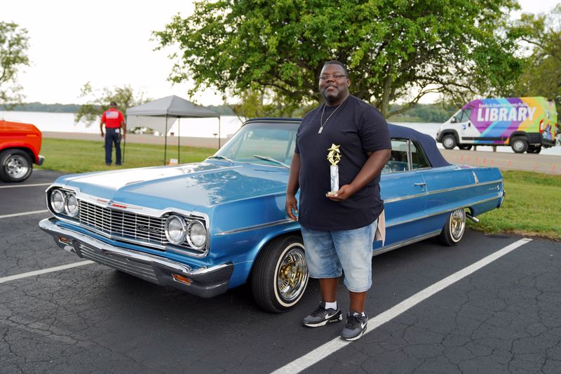 man standing next to blue car holding trophy