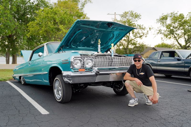man next to aqua colored car with trophies