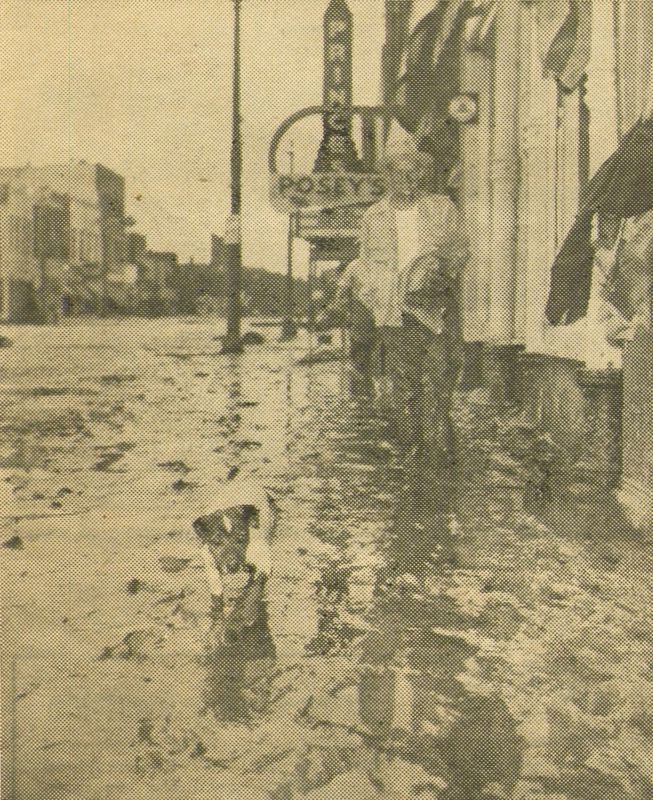 A black and white image from a special edition of the Topeka Daily Capital showing a man and his dog walking through the mud-covered sidewalks of North Topeka