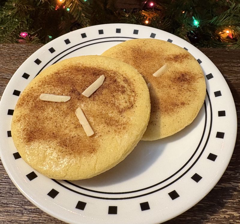 A color photograph of two light colored cookies dusted with cinnamon sugar and topped with three slivers of almonds