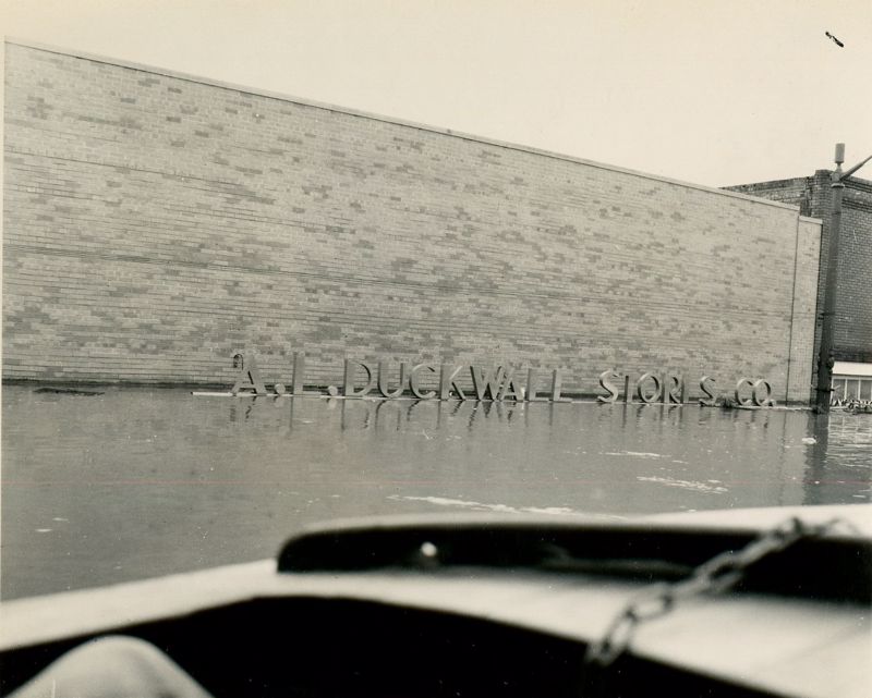A black and white photo taken from a boat during the 1951 flood showing the A.L. Duckwall store sign sitting just above the water