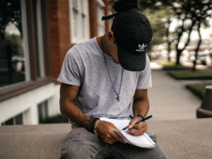 Man writing in notebook while sitting on a concrete ledge outside