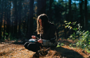 Woman crouched in a forest setting with notebook and pen in hand