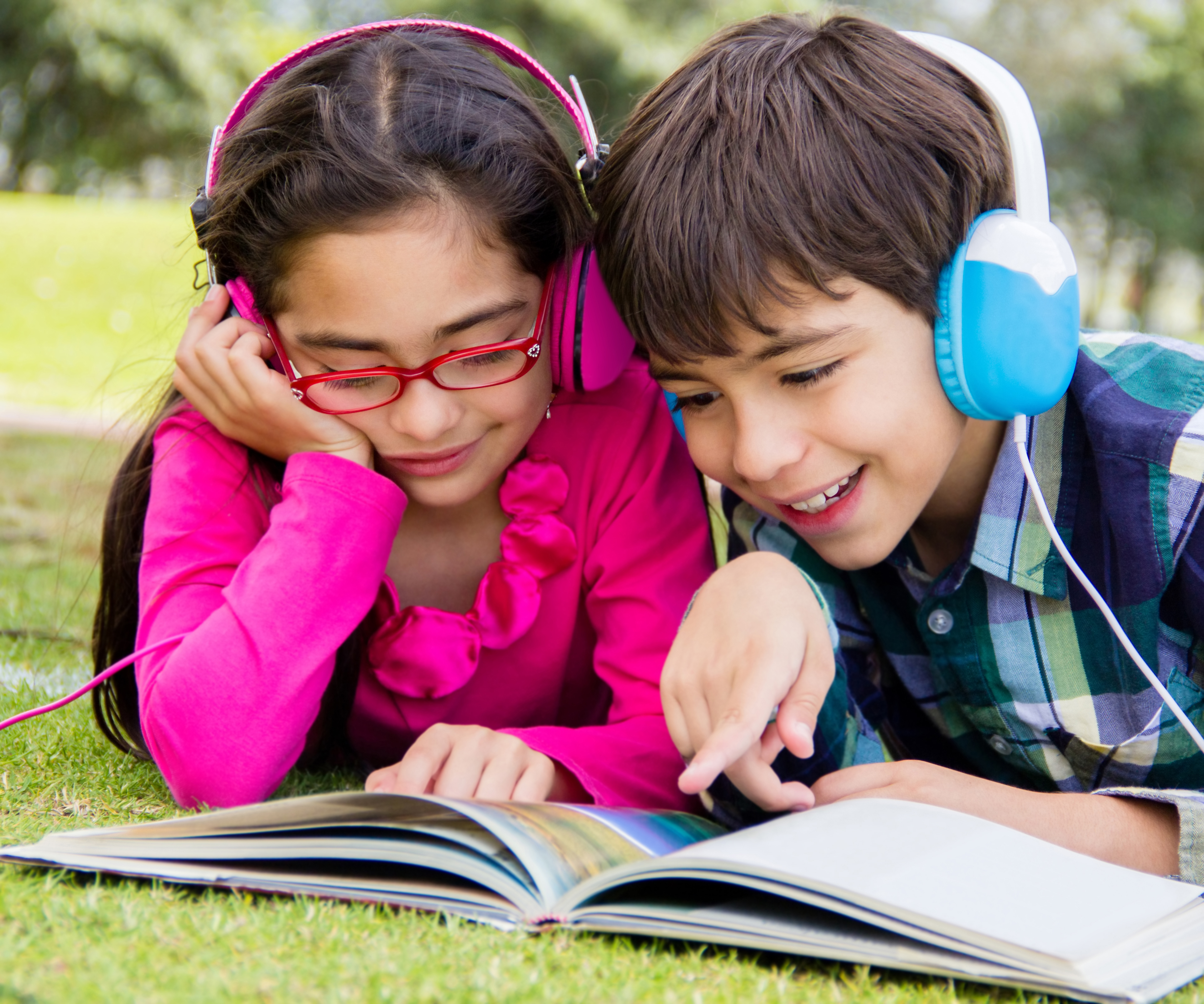 Happy kids reading at the park and listening to audiobook