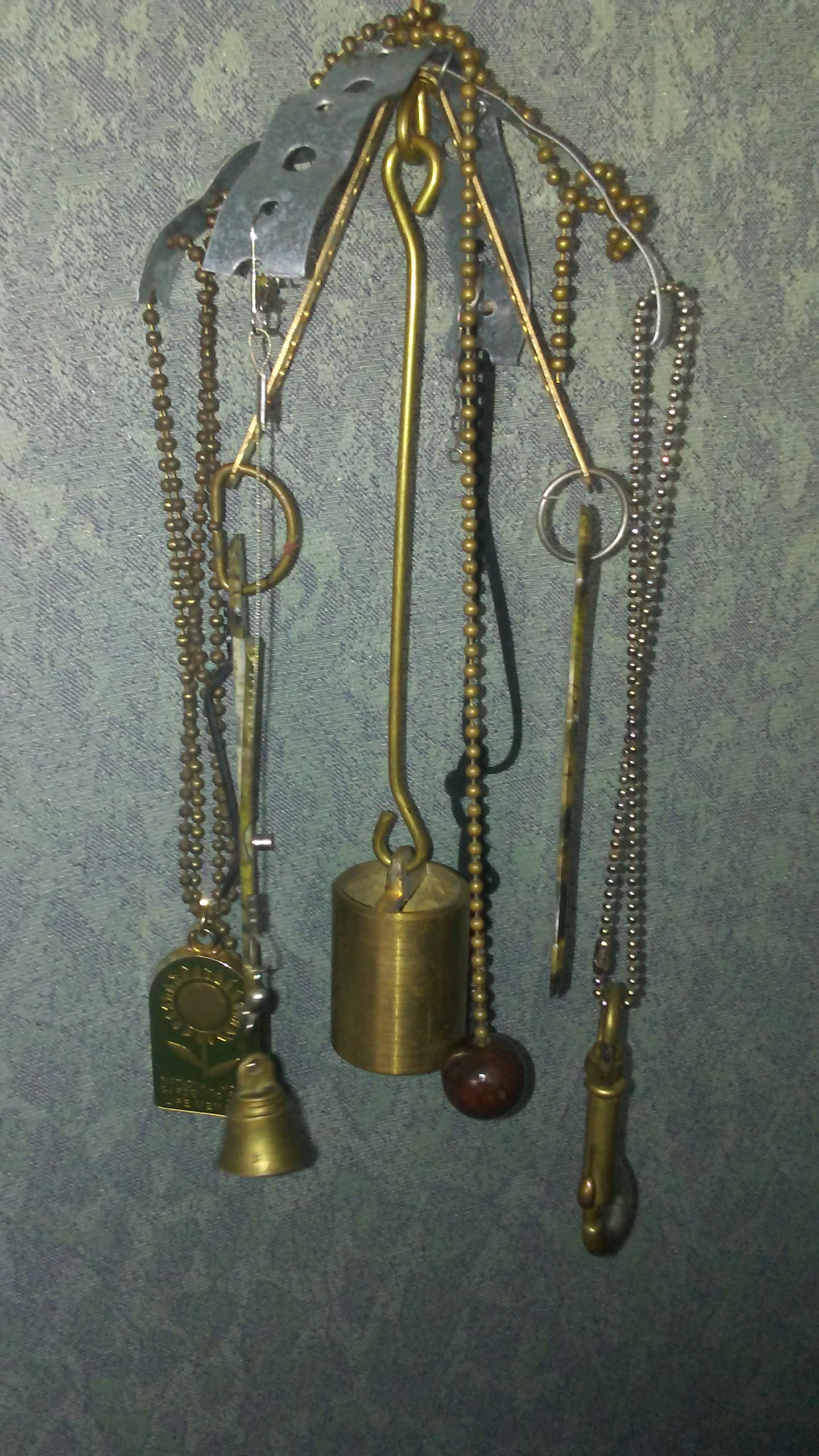 Metal Wind Chime Made of Found Objects Including Brass weight, Clamps, Lamp chain, Green and Brass Key fob, Brass Bell, Green Camo Pocket Knife Parts.