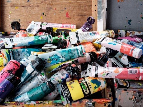 A pile of various colors of acrylic paints in tubes on a messy art desk