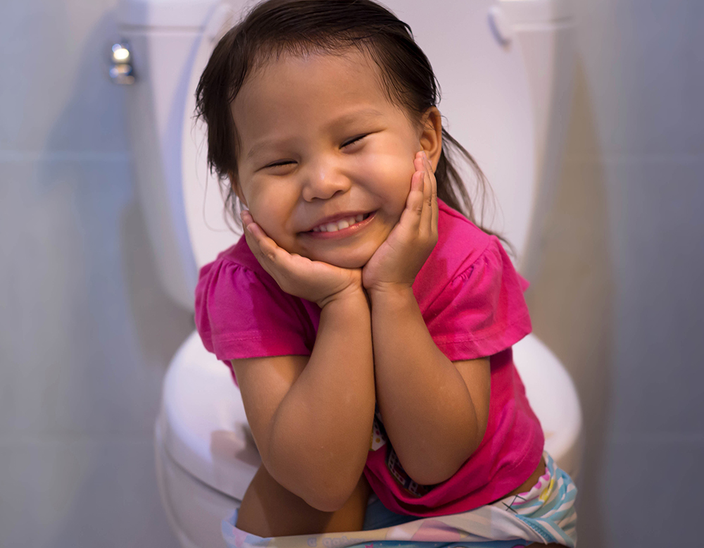 Happy little girl proud of sitting on the toilet at home.