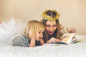 Mother and cute little child reading in bed. Having fun in imaginary land.