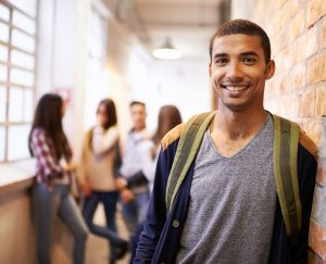 Portrait of a handsome young male student leaning against a wall with his friends in the background